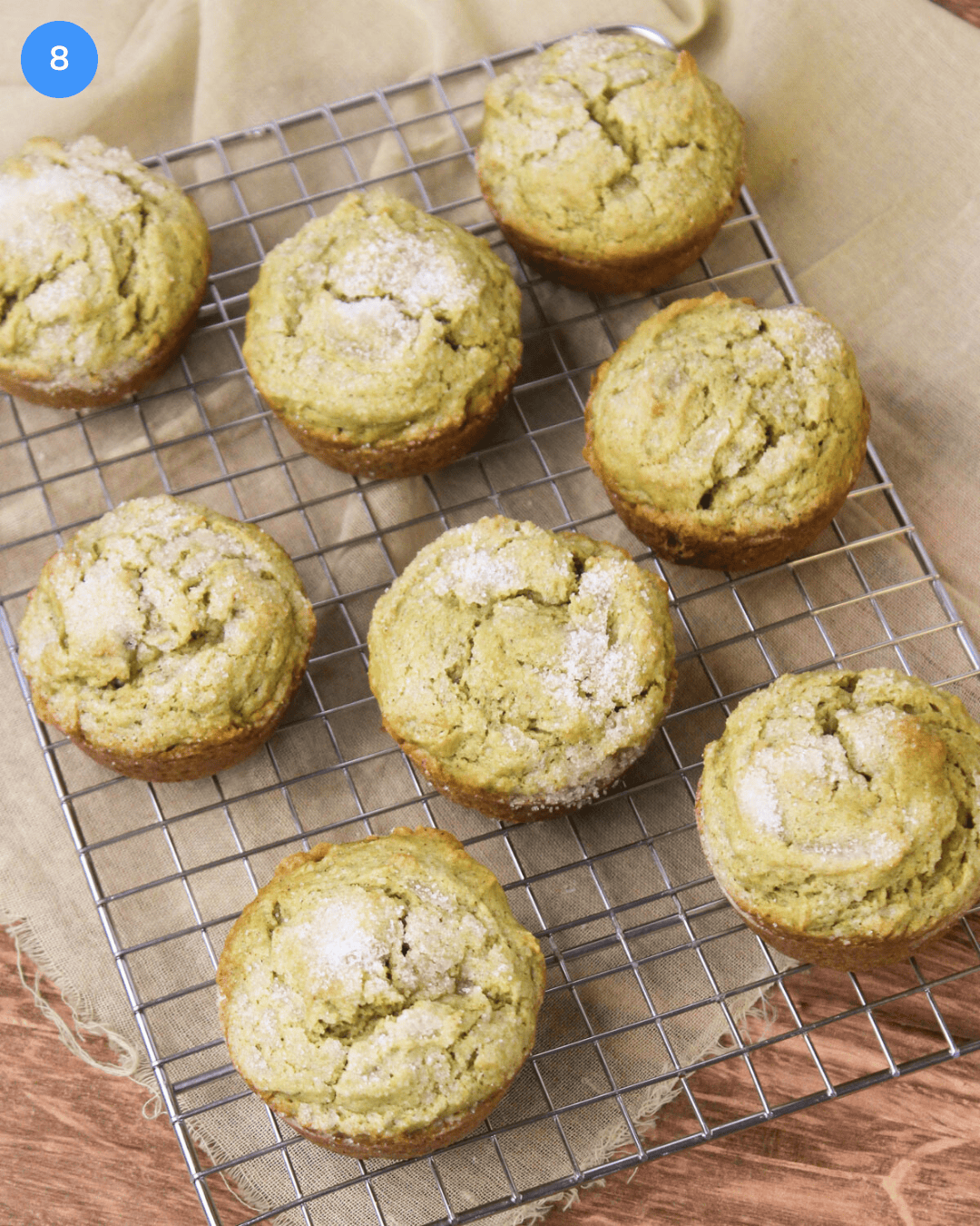 A wire cooling rack of freshly baked cinnamon avocado muffins sprinkled with sugar on top.