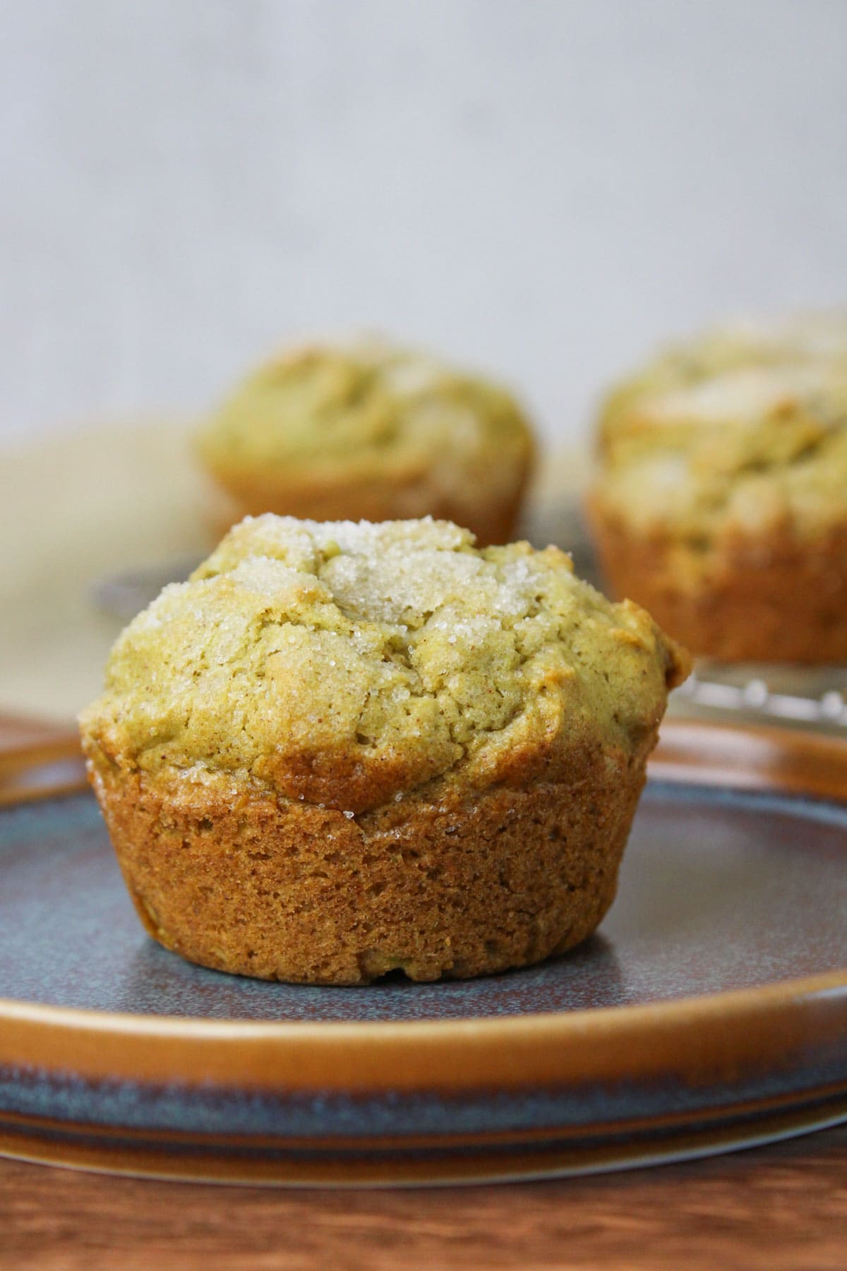 A fluffy cinnamon avocado muffin on a blue stone plate with more muffins in the background.