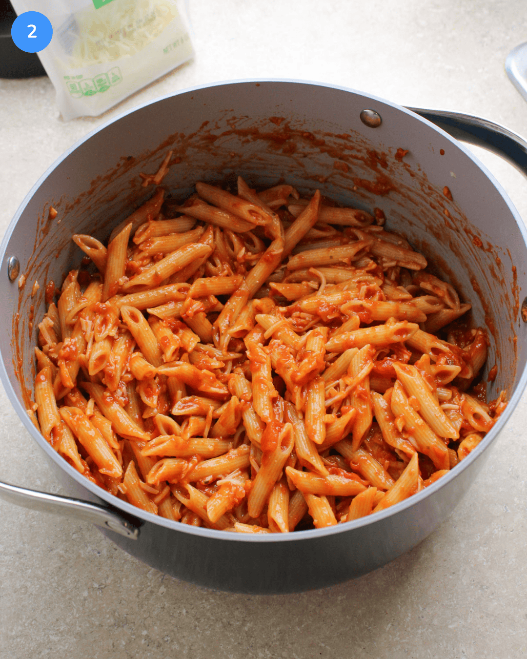A large ceramic pot filled with penne pasta that's been tossed with red sauce and shredded mozzarella.
