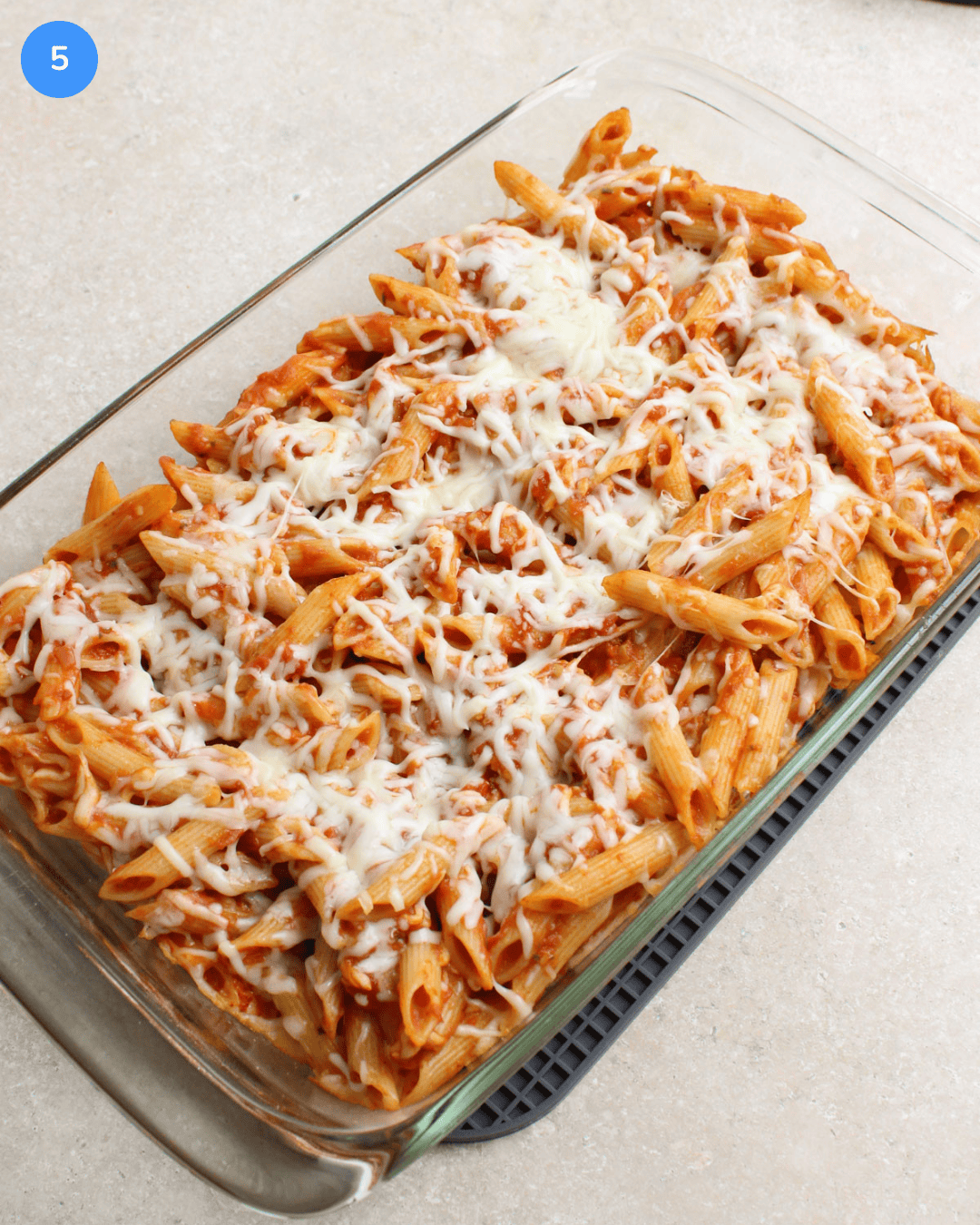 A 9 by 13 glass baking dish full of freshly baked penne pasta with red sauce and shredded mozzarella cheese.
