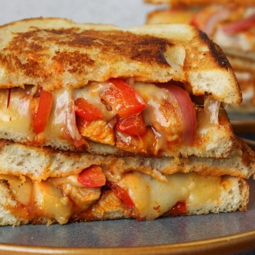 A cheesy chipotle chicken melt fresh off the stove with sliced red bell pepper and red onion on a blue stone plate.