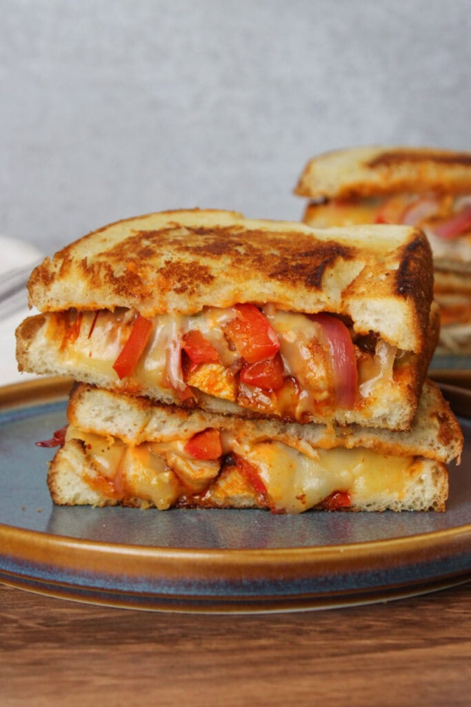 A crispy, gooey chipotle chicken melt with red bell pepper and red onion on sourdough, cut in half and served on a blue stone plate.