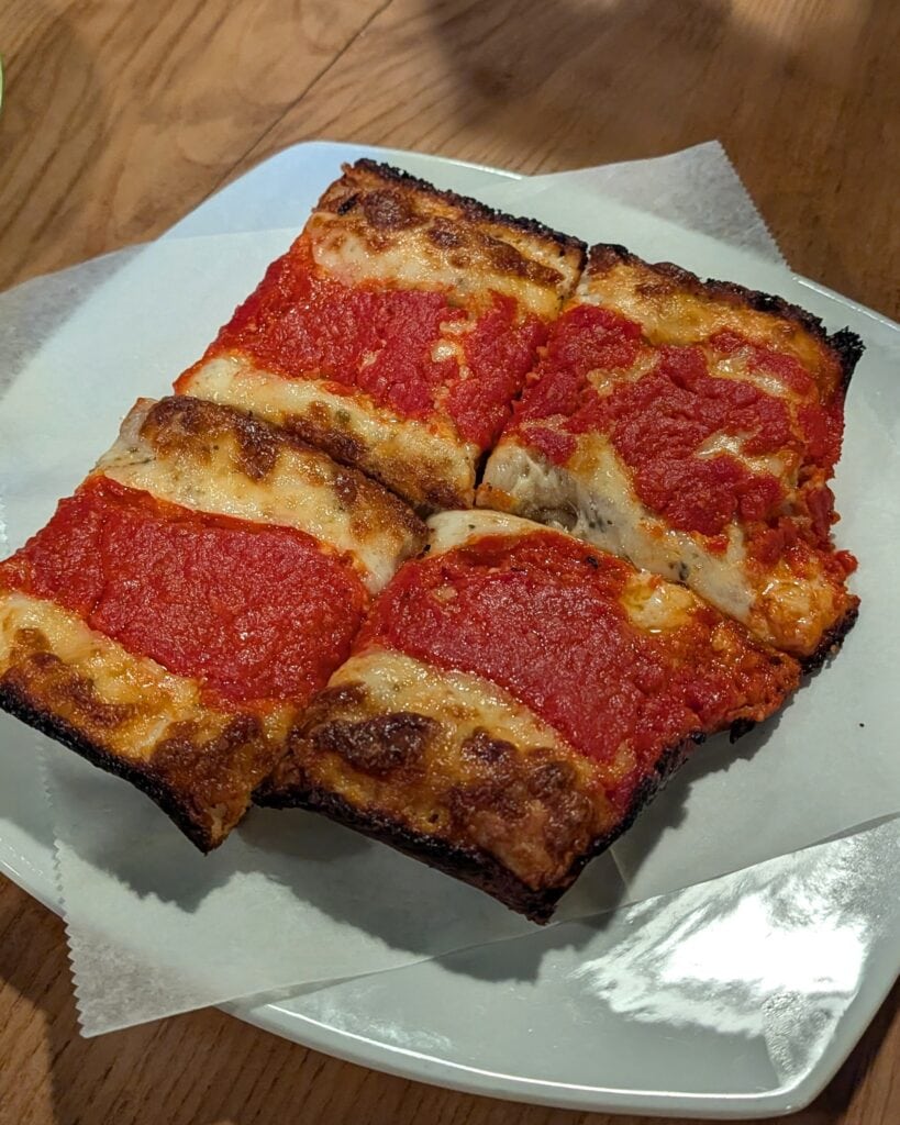Four large square slices of Detroit style pizza on a white ceramic plate.