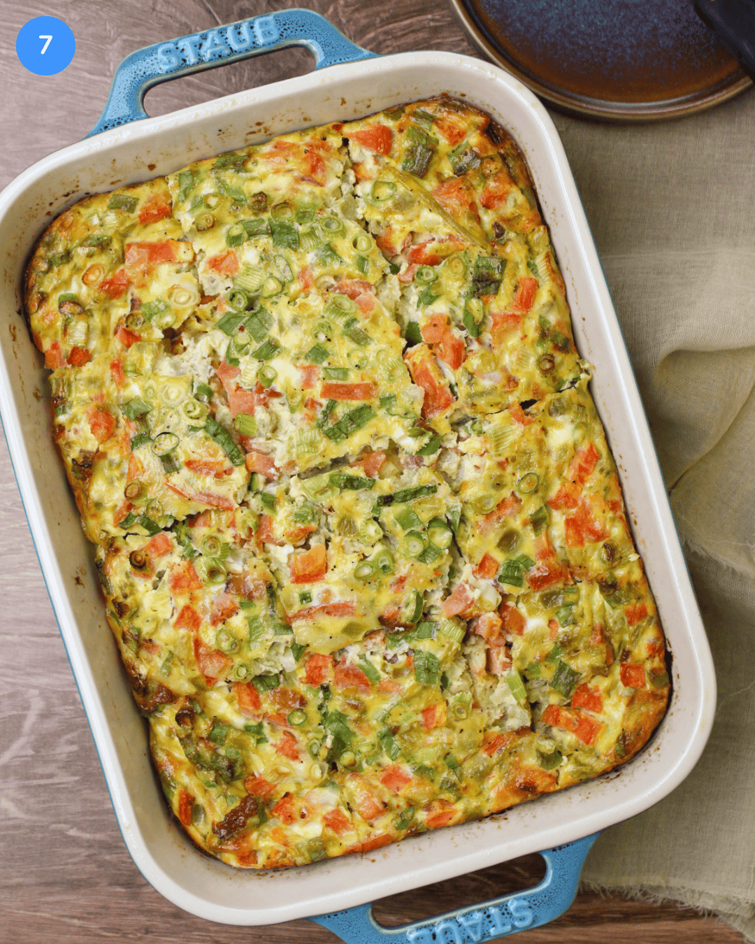 Freshly baked egg casserole with green chilies, tomato, scallions, bacon, and cheese, sliced into 12 squares inside a rectangular baking dish.