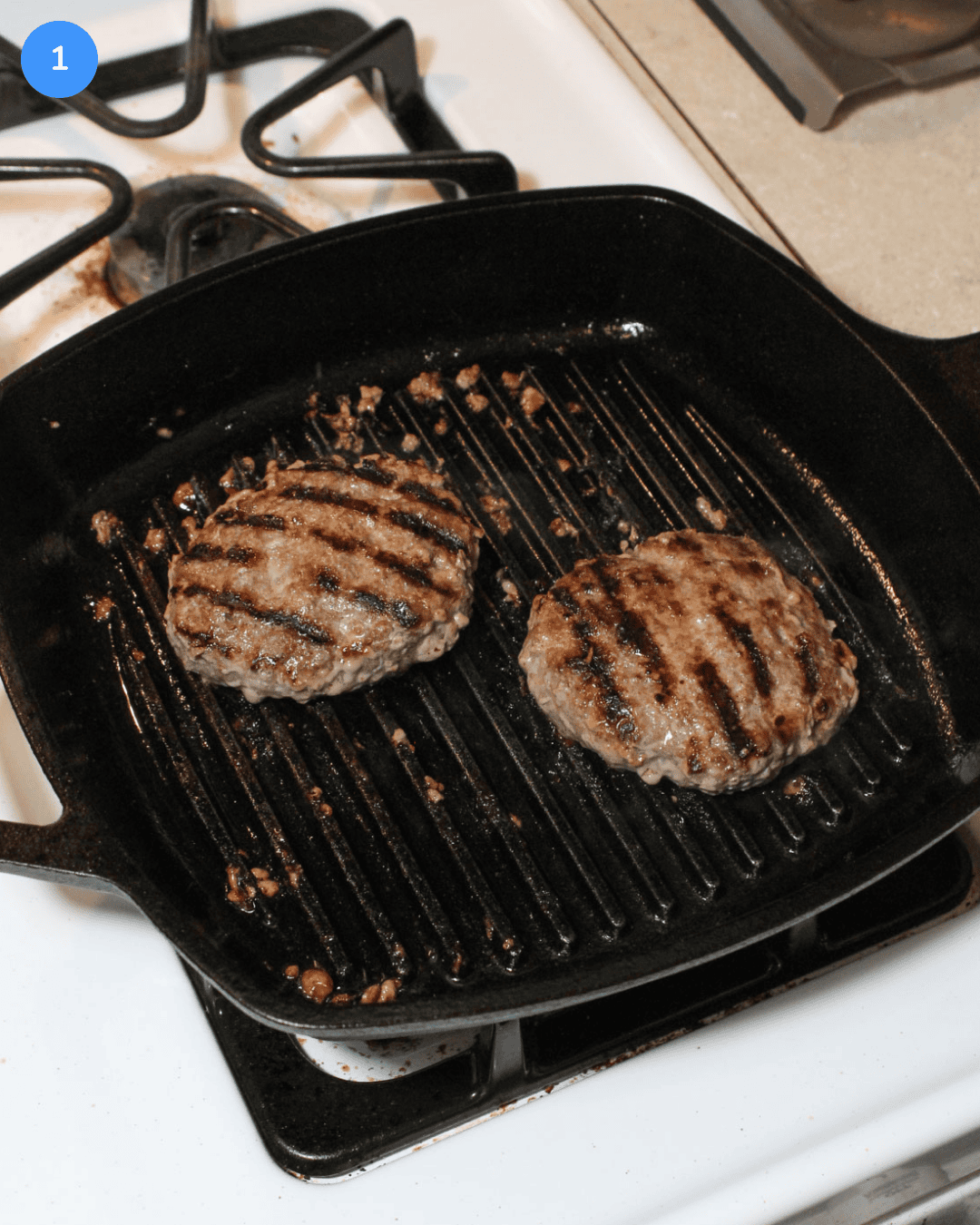Two burger patties cooking on a cast iron grill pan on the stove.