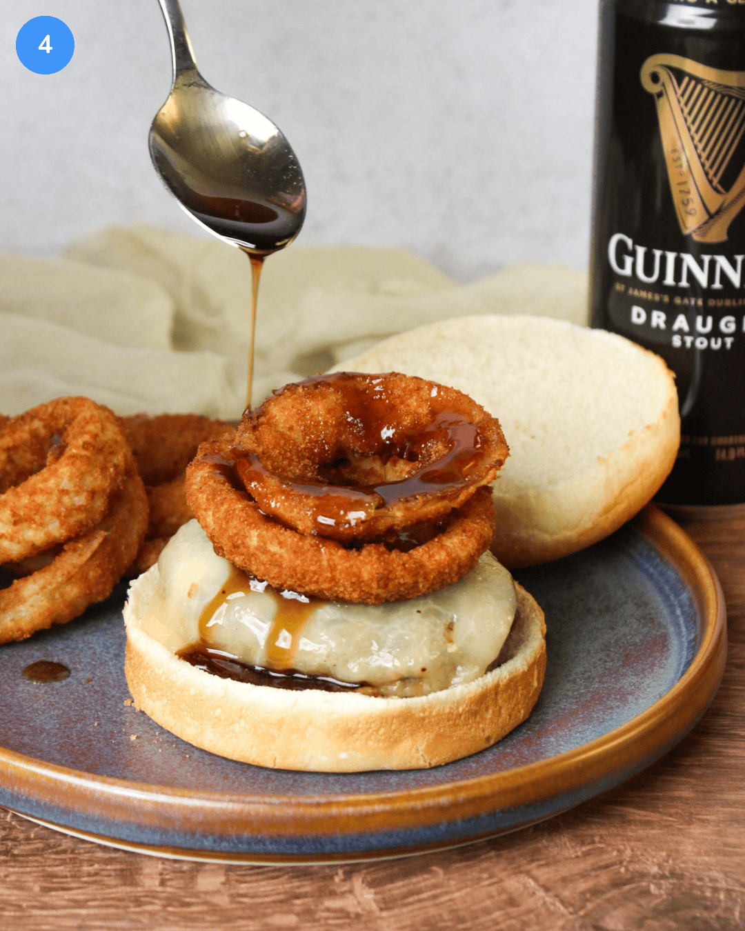 A cheeseburger topped with crispy onion rings being drizzled with Guinness glaze.