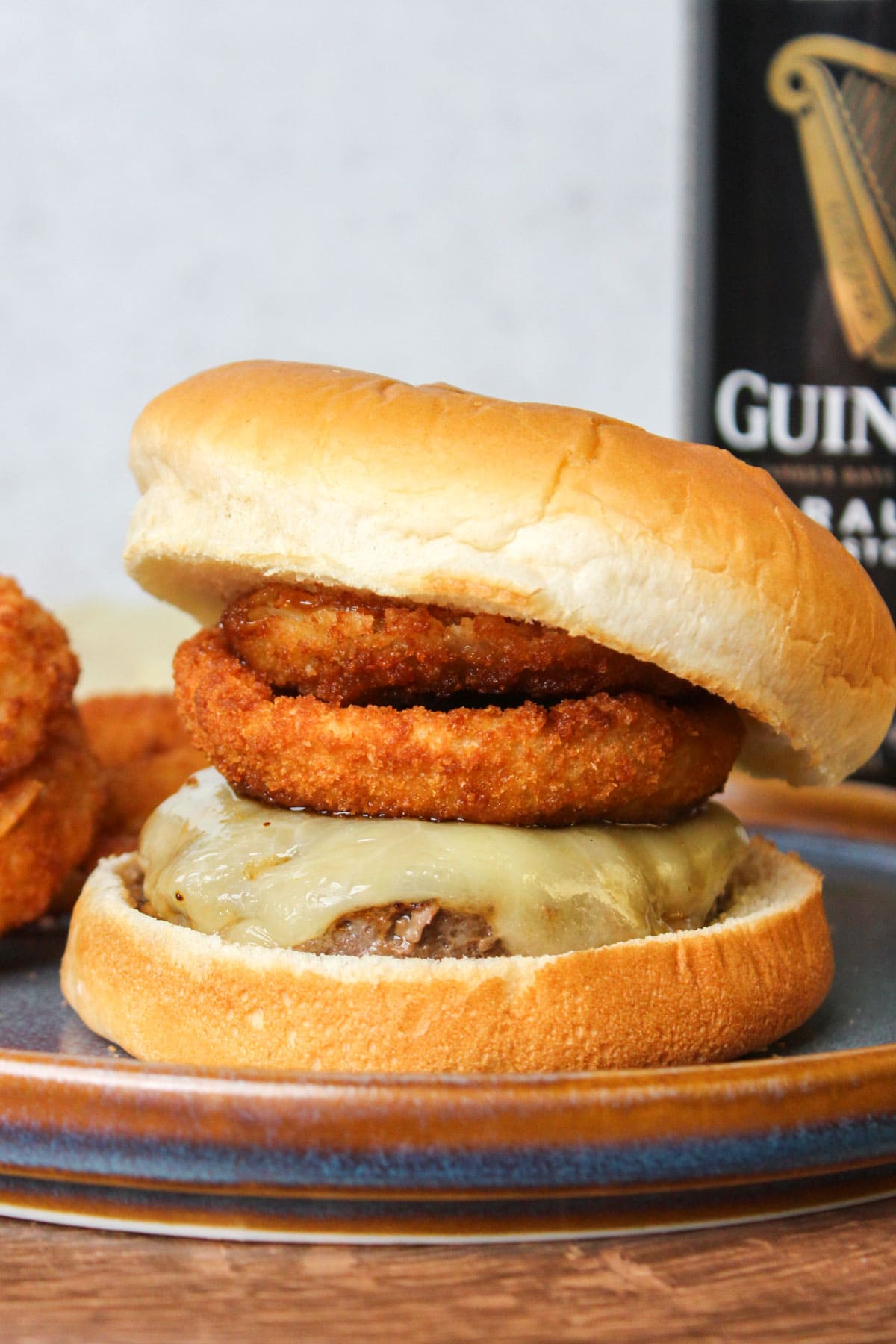 A freshly made Guinness burger topped with white cheddar, crispy onion rings, and Guinness glaze with a can of Guinness beer.