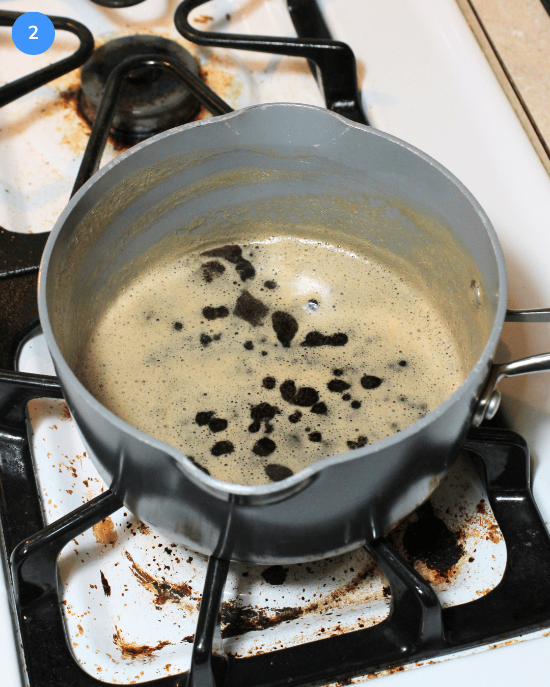A small ceramic saucepan with a Guinness brown sugar glaze thickening in it on the stove.