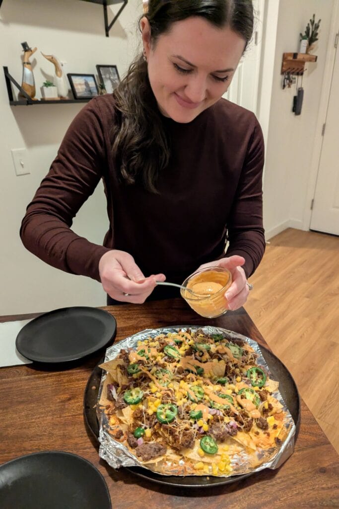 Nicole drizzling chipotle mayo on a platter of chorizo nachos.