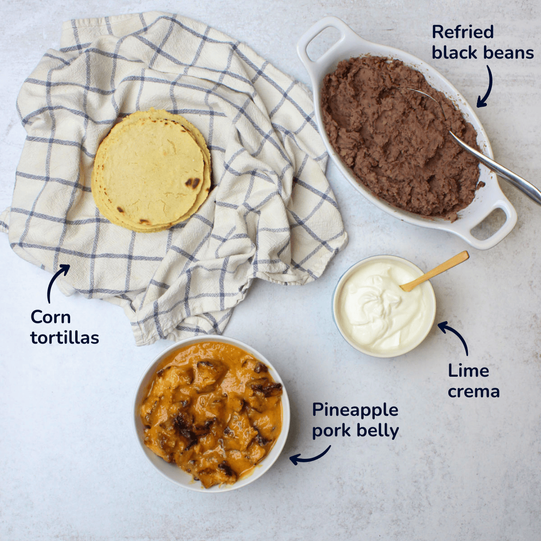 Ingredients for crispy pork belly tacos: pineapple pork belly, corn tortillas, refried black beans, and lime crema.