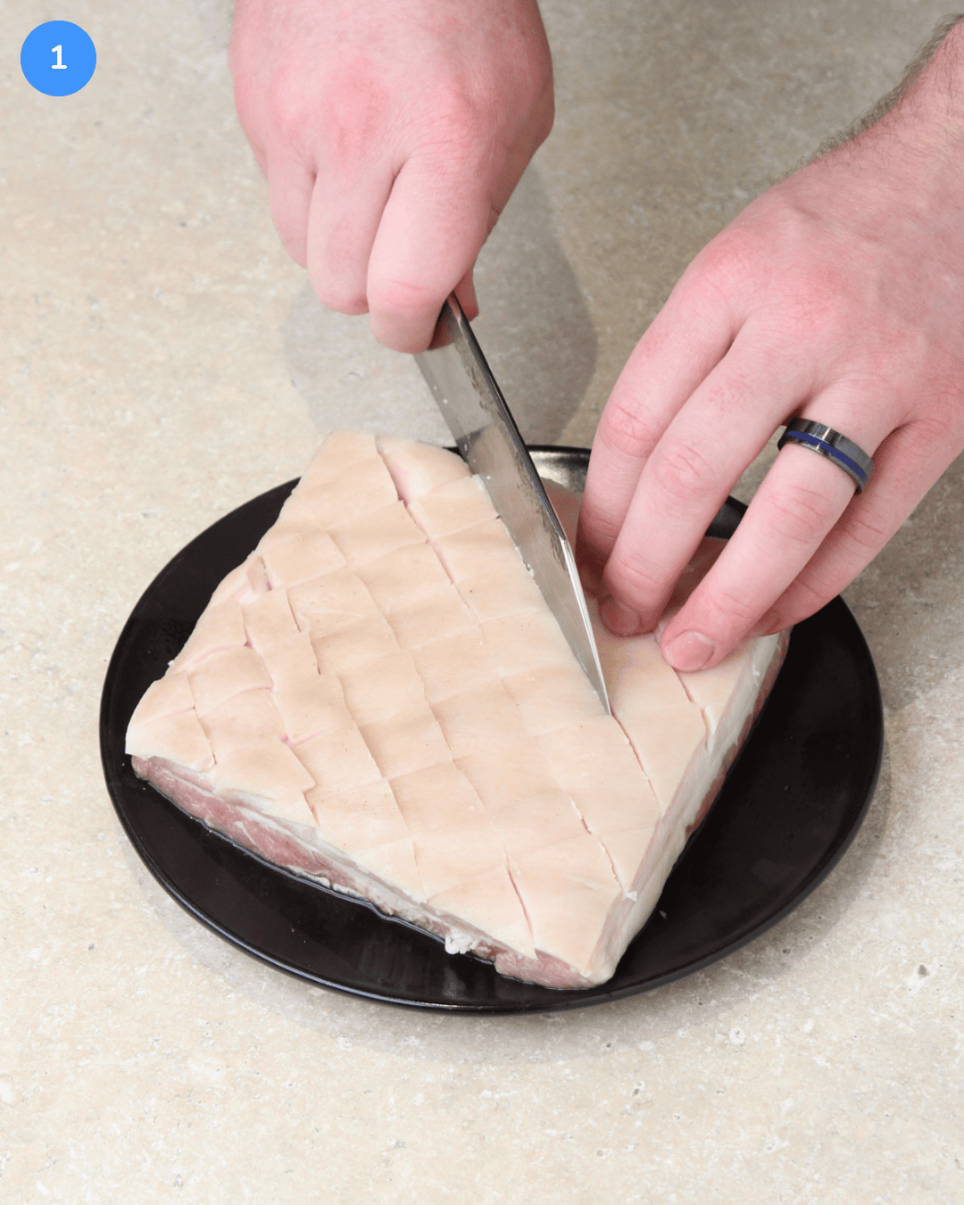 A slab of raw pork belly being scored in a cross-hatch pattern on the skin.