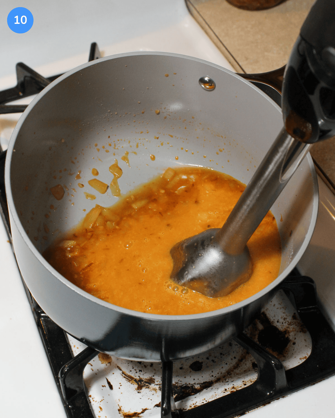 A pineapple chipotle sauce in a ceramic saucepan being pureed with an immersion blender.