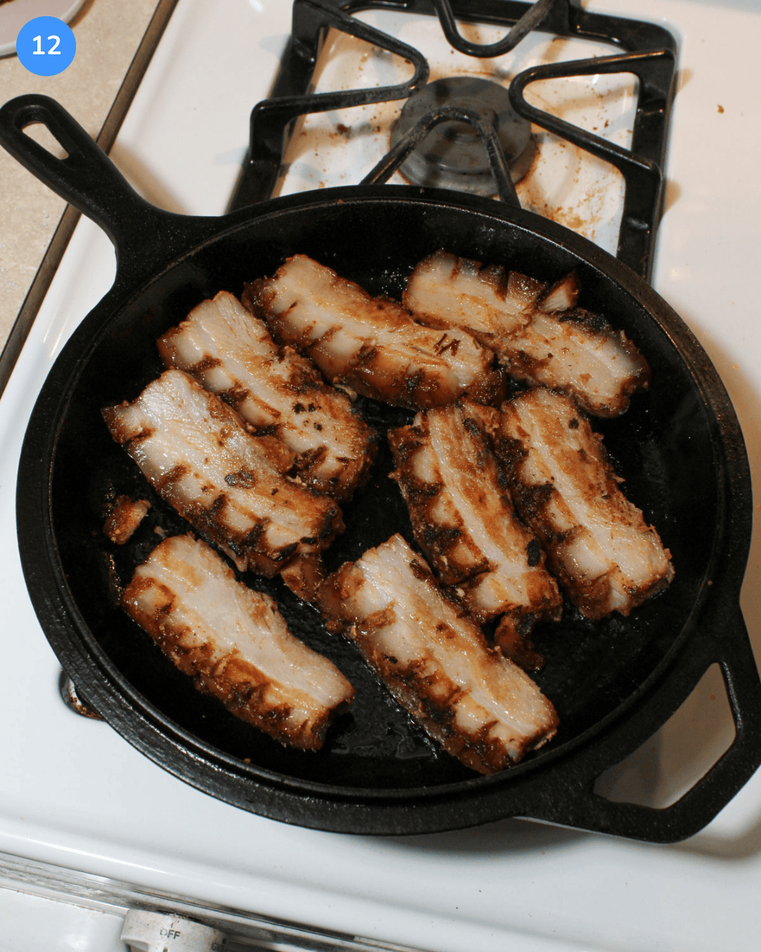 Slabs of pork belly crisping in a cast iron skillet on the stove.