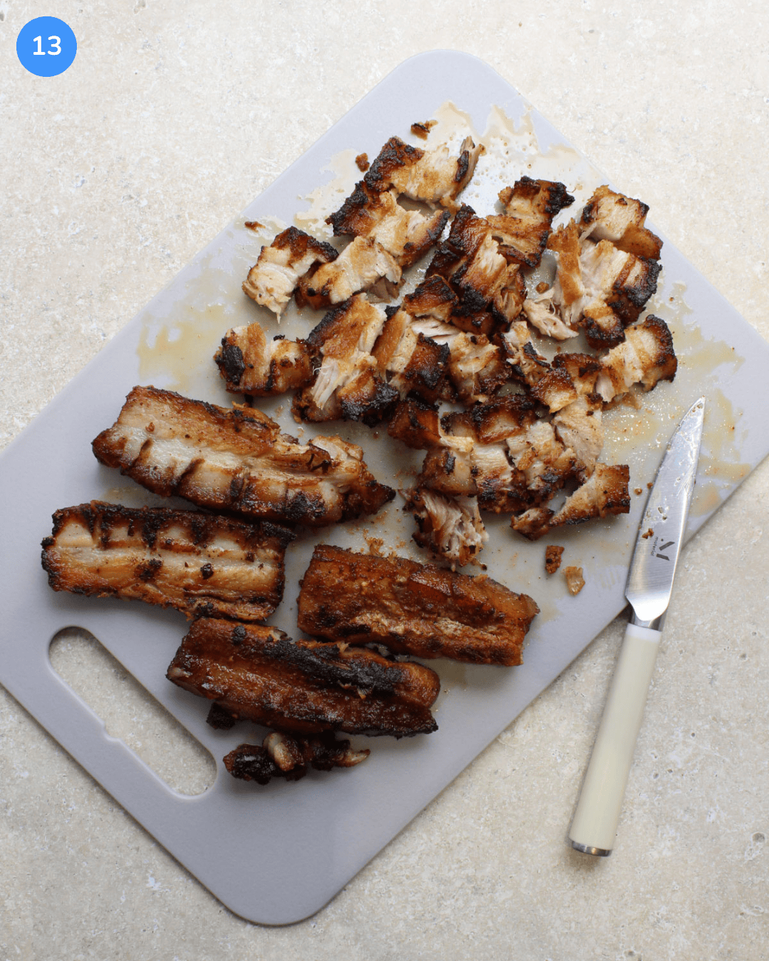 Crispy pork belly being sliced into bite-size pieces on a cutting board.