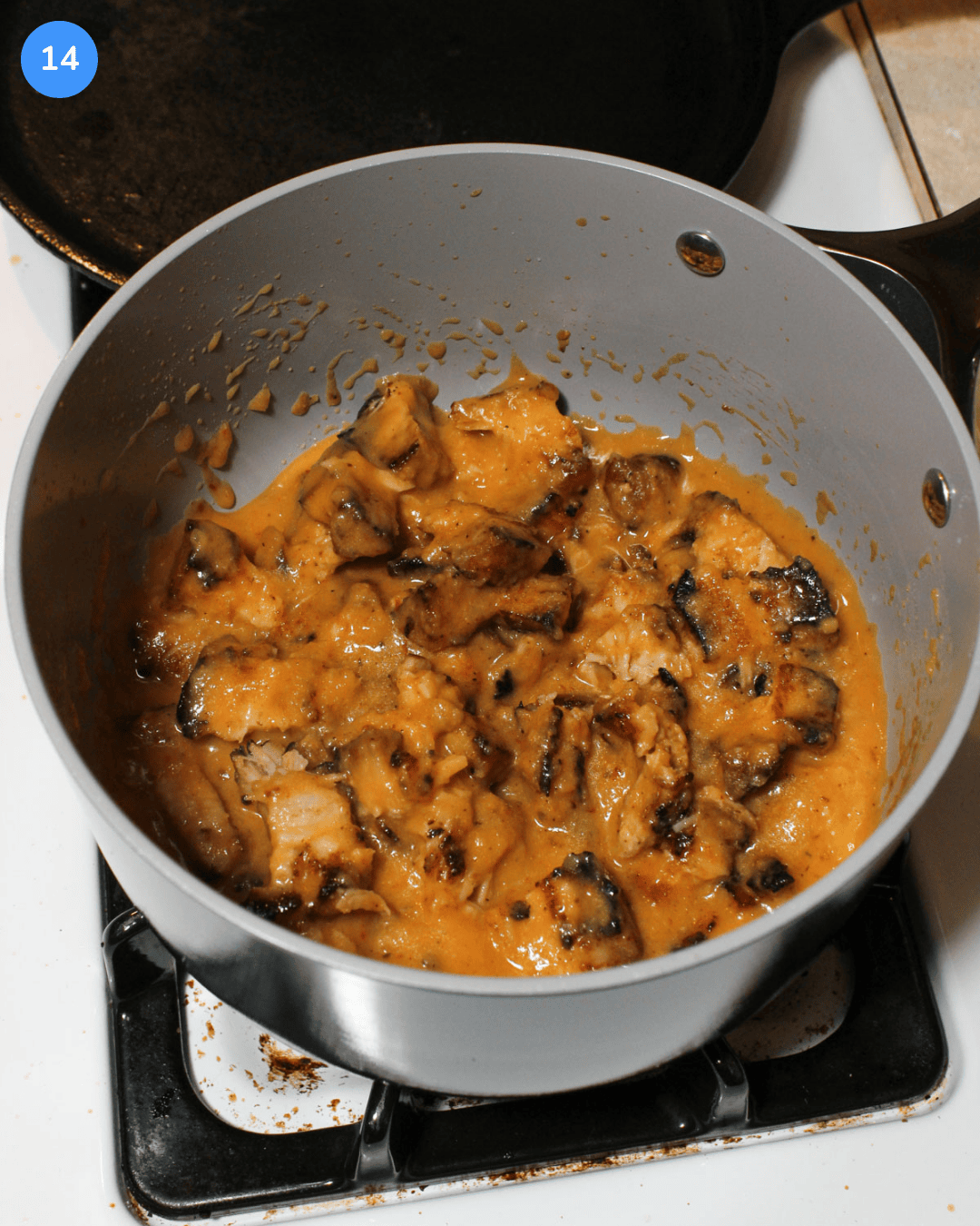 A saucepan with pineapple chipotle sauce and crispy pork belly chunks in it on the stove.