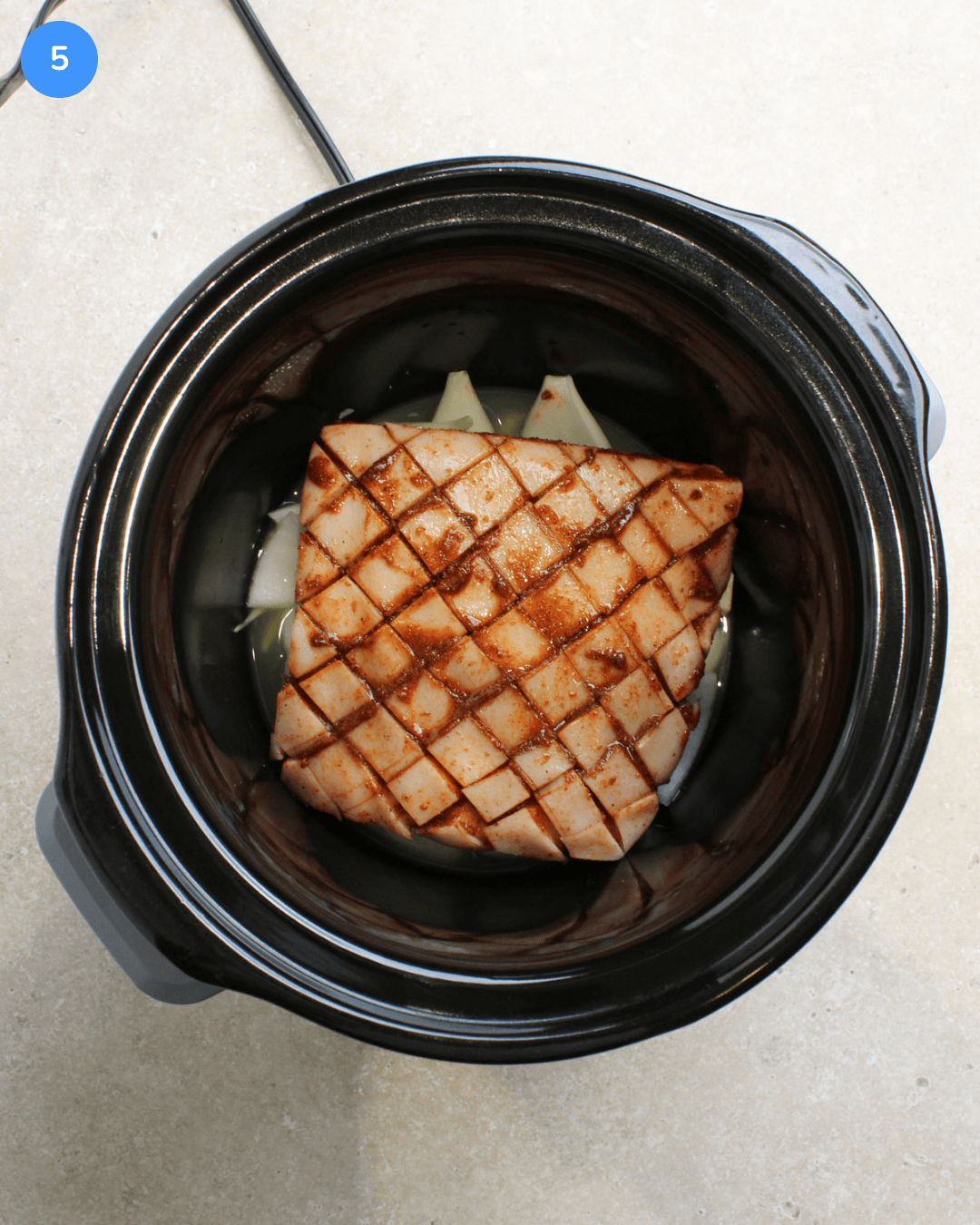 A black crockpot with a slab of raw pork belly that's been rubbed with a spicy paste.