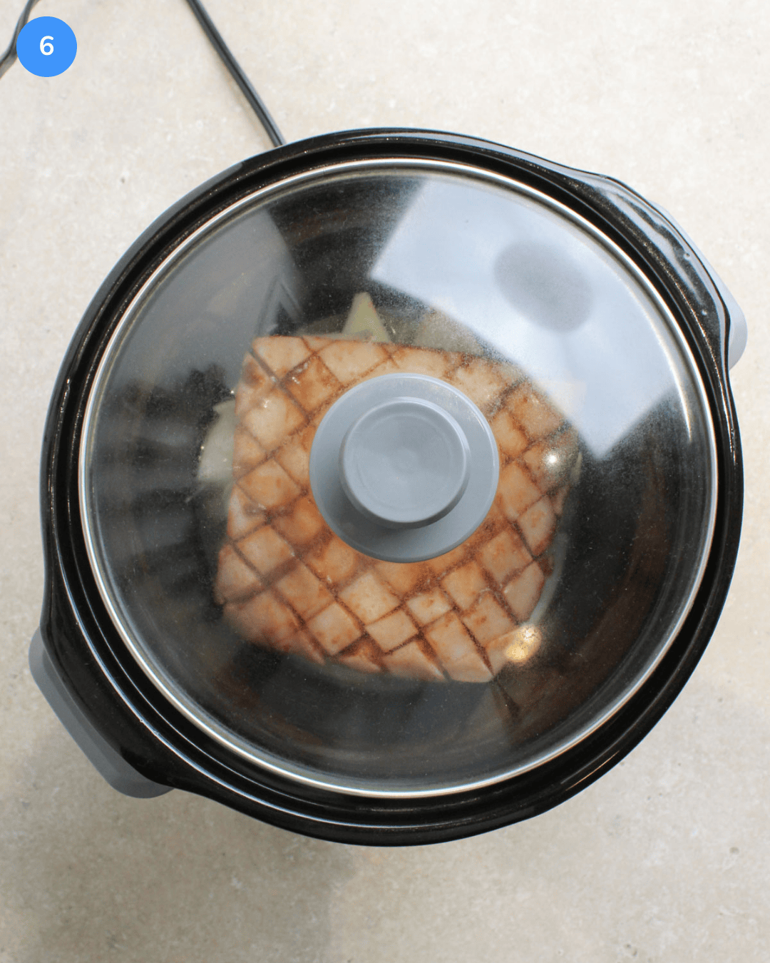 A black crockpot with pork belly and aromatics inside it, with the lid on.