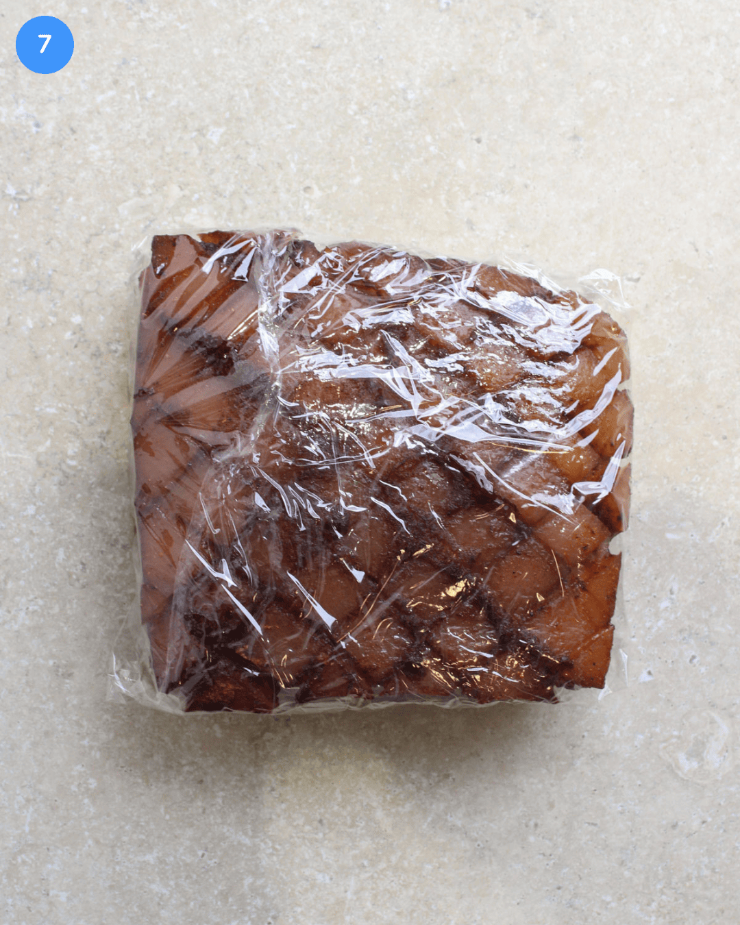 A slab of freshly made crockpot pork belly that's been cooled and wrapped in plastic wrap.
