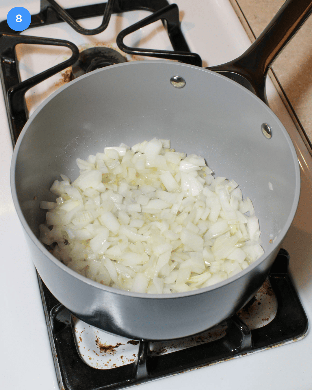 A ceramic nonstick saucepan with diced white onion and minced garlic cooking in it on the stove.