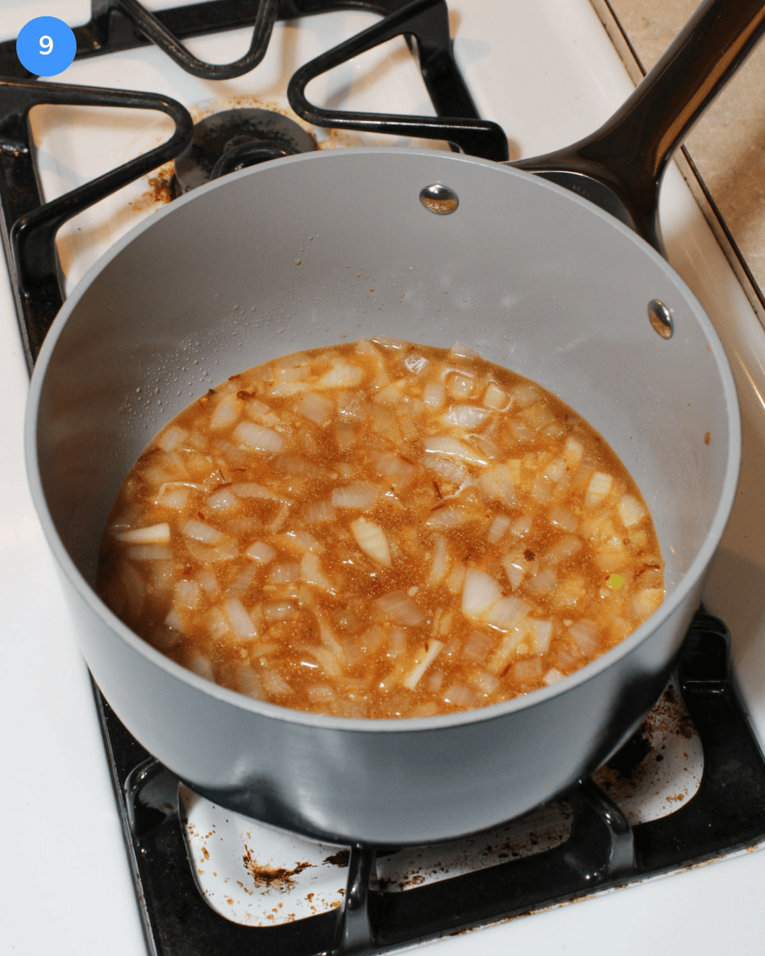 A ceramic nonstick saucepan with onion, garlic, pineapple juice, lime juice, and chipotle puree in it simmering on the stove.