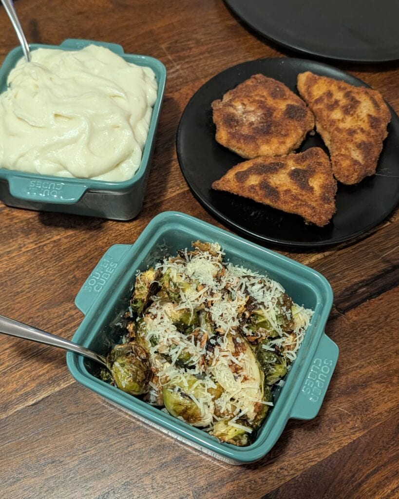 A plate of crispy chicken and two green ceramic square serving dishes with brussel sprouts and mashed potatoes.