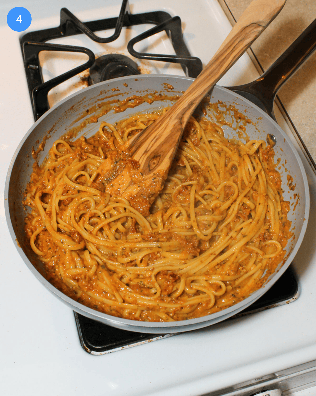 Freshly cooked sun dried tomato pesto pasta in a frying pan on the stove after tossing it together.