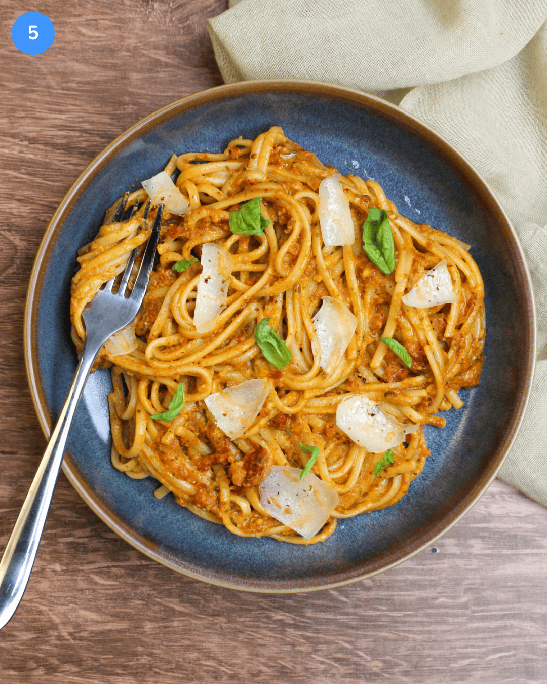 A fresh plate of sun-dried tomato pesto pasta, garnished with fresh basil leaves and parmesan shards.