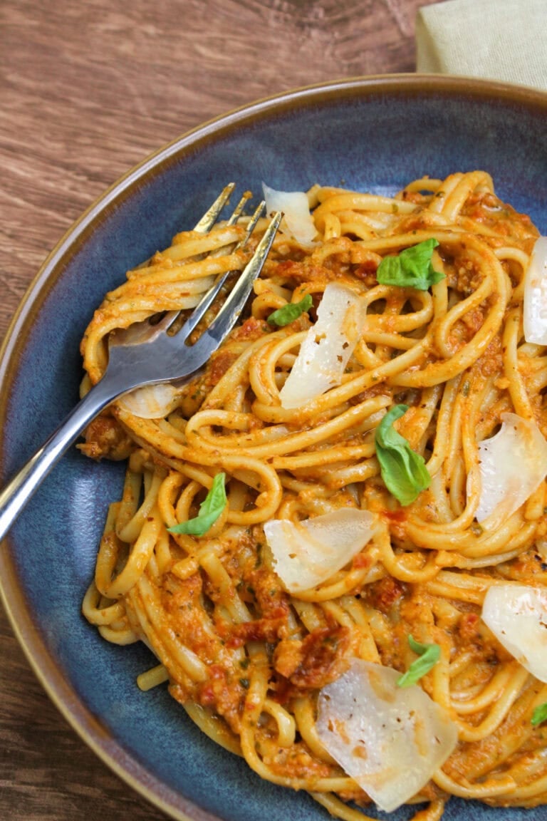 A freshly made bowl of sun-dried tomato pesto linguine, topped with fresh basil and parmesan shards.