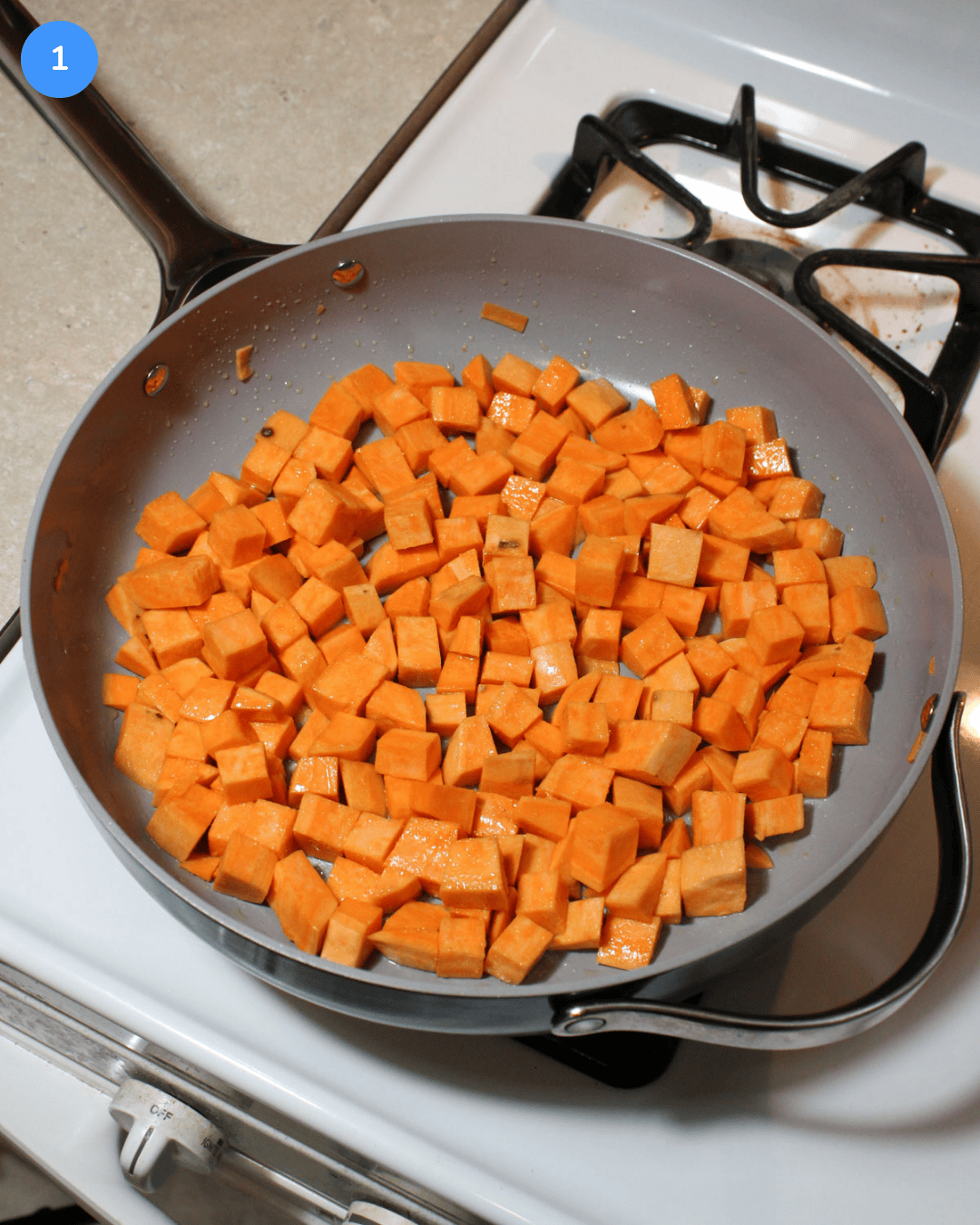 Cubed sweet potato cooking in a large ceramic saute pan on the stove.