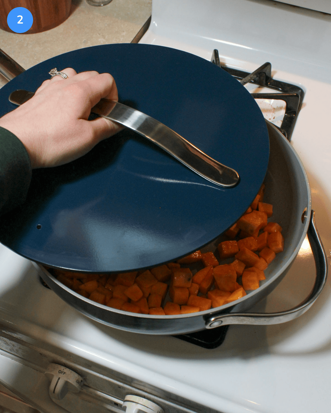 Placing a lid on a large ceramic saute pan on the stove to steam cubed sweet potatoes.