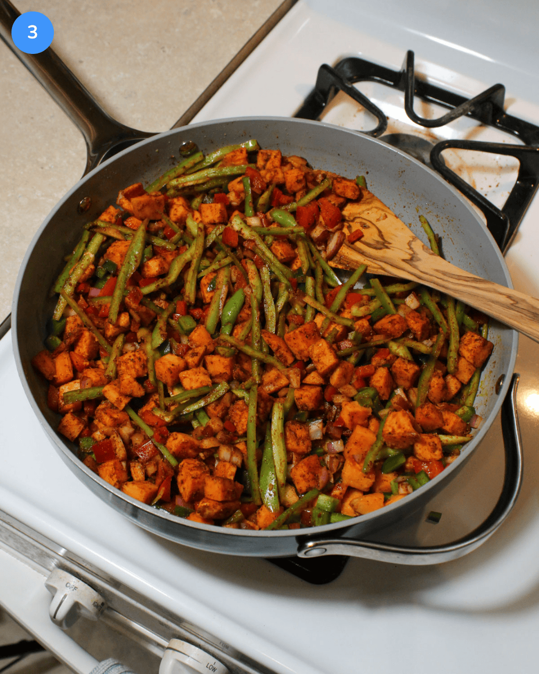 A large ceramic saute pan filled with cubed sweet potatoes and peppers tossed in taco seasoning.