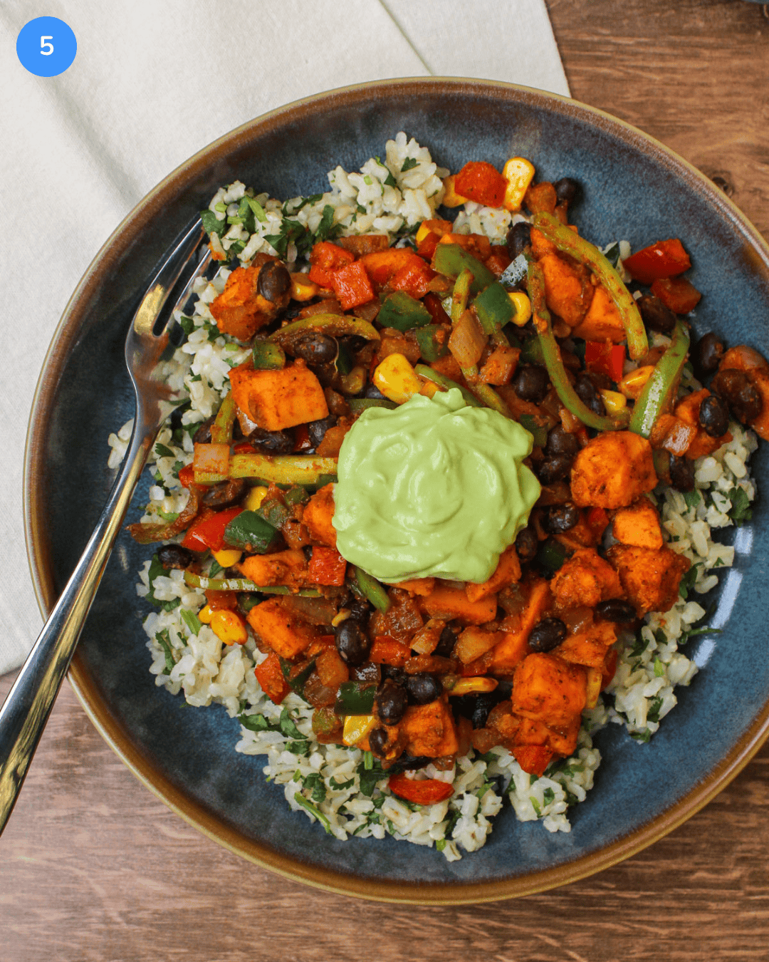 A sweet potato taco bowl with cilantro lime rice, peppers, onion, corn, black beans, and a dollop of avocado crema.