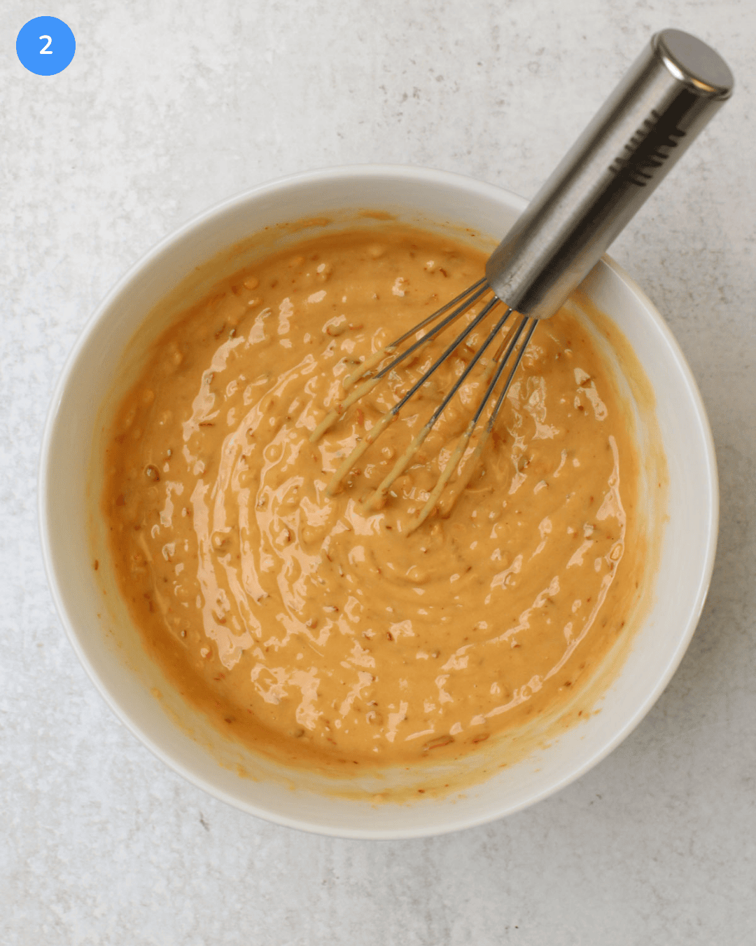 Spicy cashew butter dressing in a small white bowl with a mini whisk.