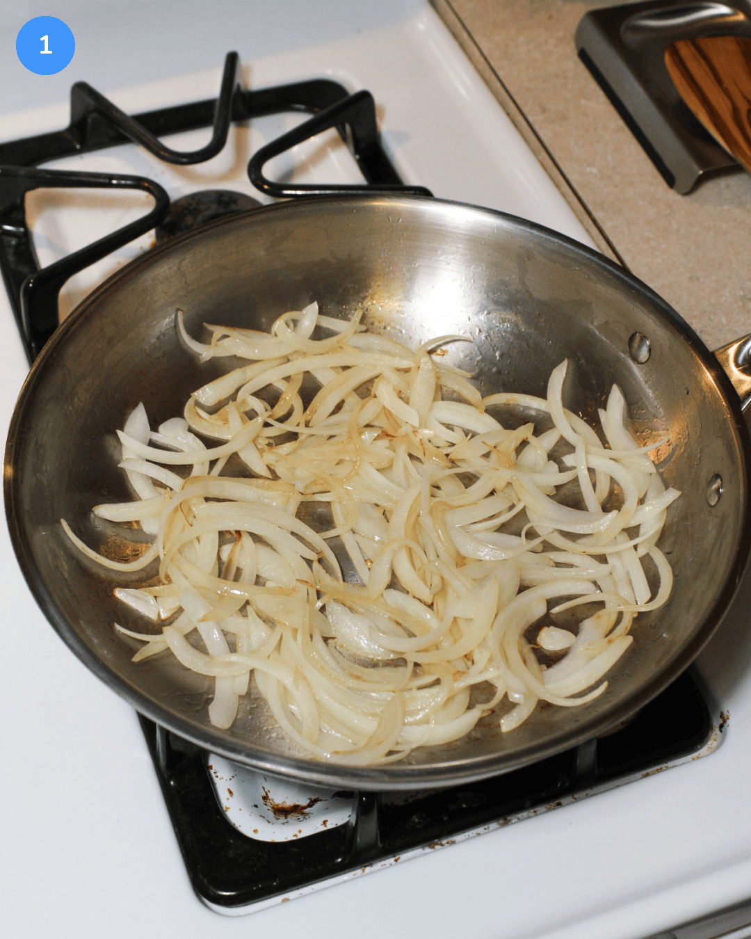 Sliced yellow onion caramelizing in a stainless steel frying pan on the stove.