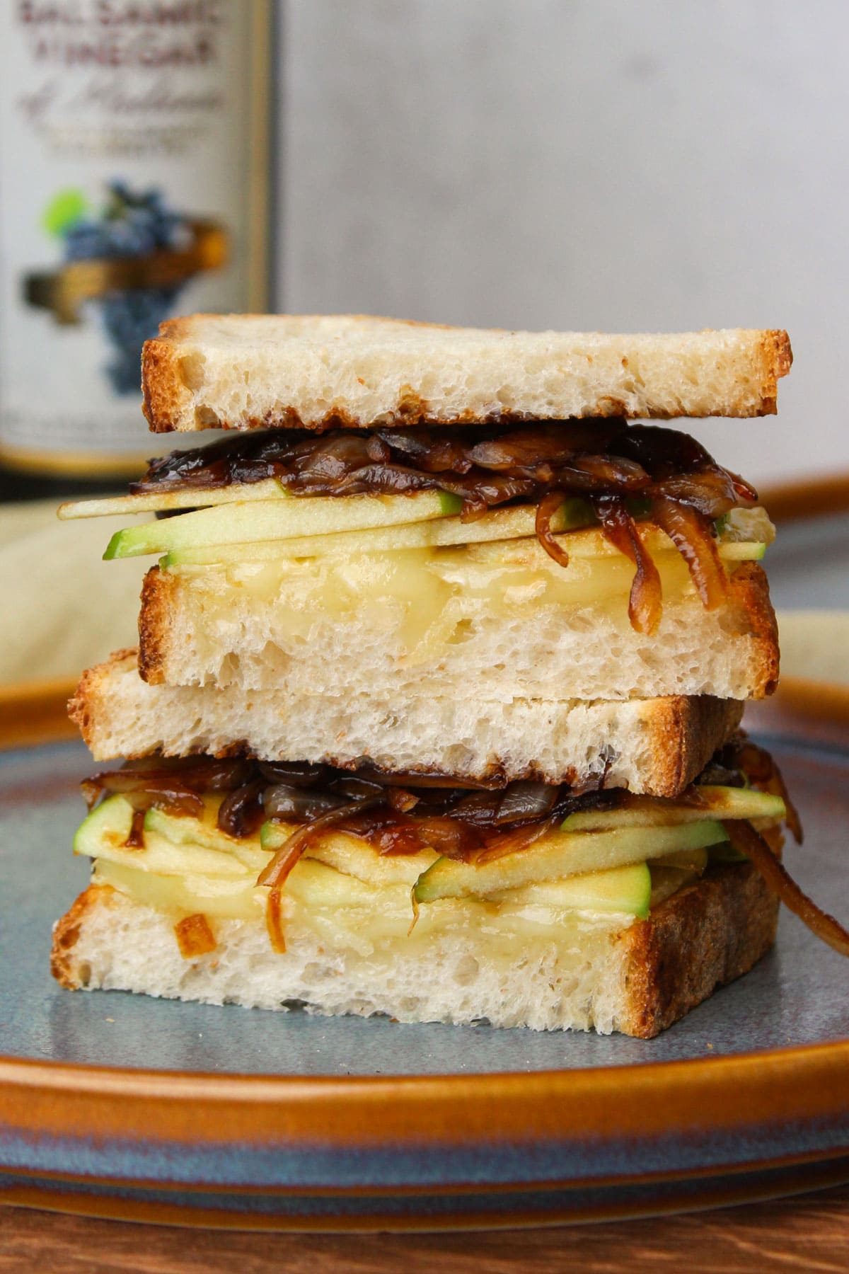 Two halves of a gooey baked brie sandwich on Italian bread with sliced green apple and balsamic onions on a blue stone plate.