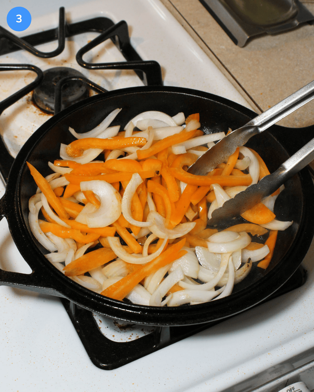 Sliced onion and orange bell pepper cooking in a cast iron skillet on the stove.