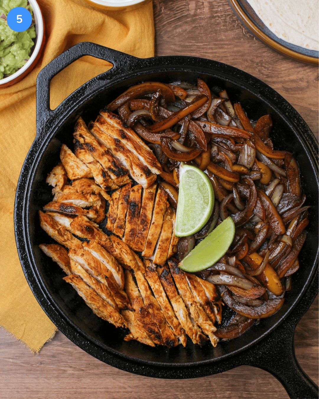 A cast iron skillet serving freshly cooked fajita chicken with peppers, onions, and lime wedges.