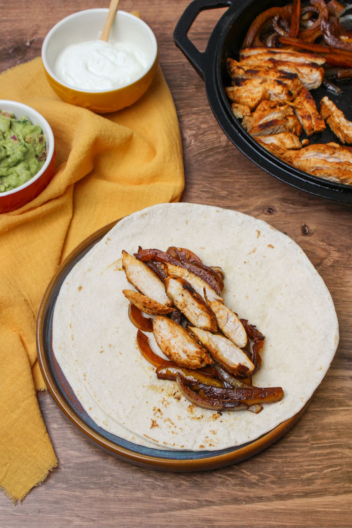 Freshly made chicken fajitas in a flour tortilla, with a skillet and bowls of greek yogurt and guacamole.