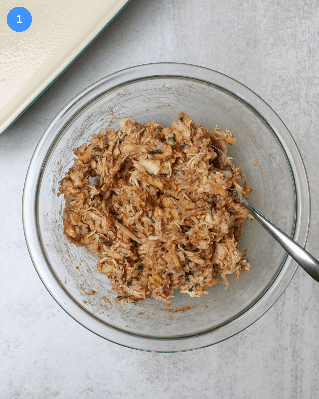 Shredded chicken, refried beans, Mexican cheese, and cilantro lime rice mixed together in a glass mixing bowl.