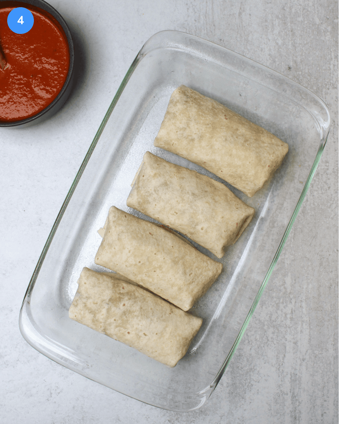 Four burritos in a glass baking dish.