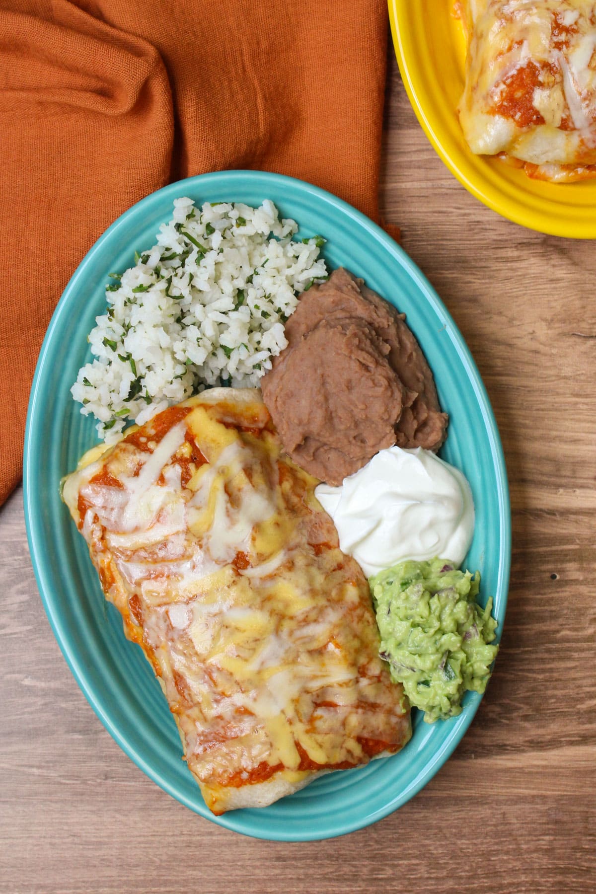 A freshly made chicken burrito ranchero plate with cilantro lime rice, refried beans, greek yogurt, and guacamole.