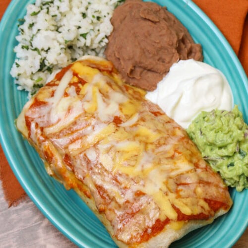 A blue ceramic plate serving a wet burrito topped with ranchero sauce and cheese.