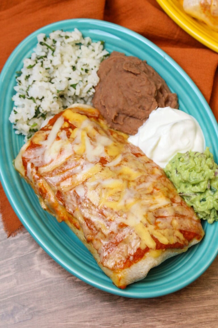 A blue ceramic plate serving a wet burrito topped with ranchero sauce and cheese.