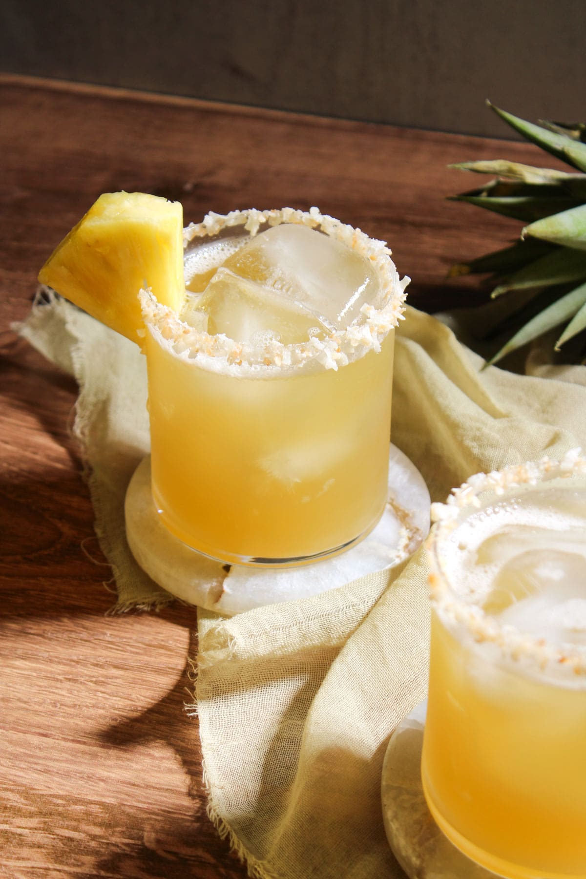 A freshly made pineapple coconut water mocktail in a rocks glass, garnished with a toasted coconut rim and a pineapple wedge.