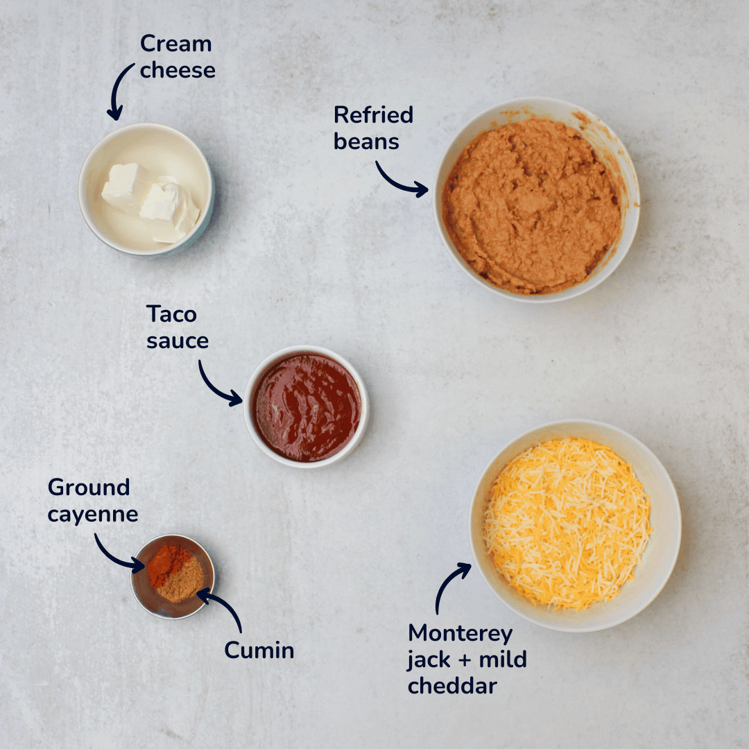 Ingredients for making Mexican bean dip: refried beans, cream cheese, taco sauce, ground cayenne, cumin, and a monterey jack and mild cheddar blend.