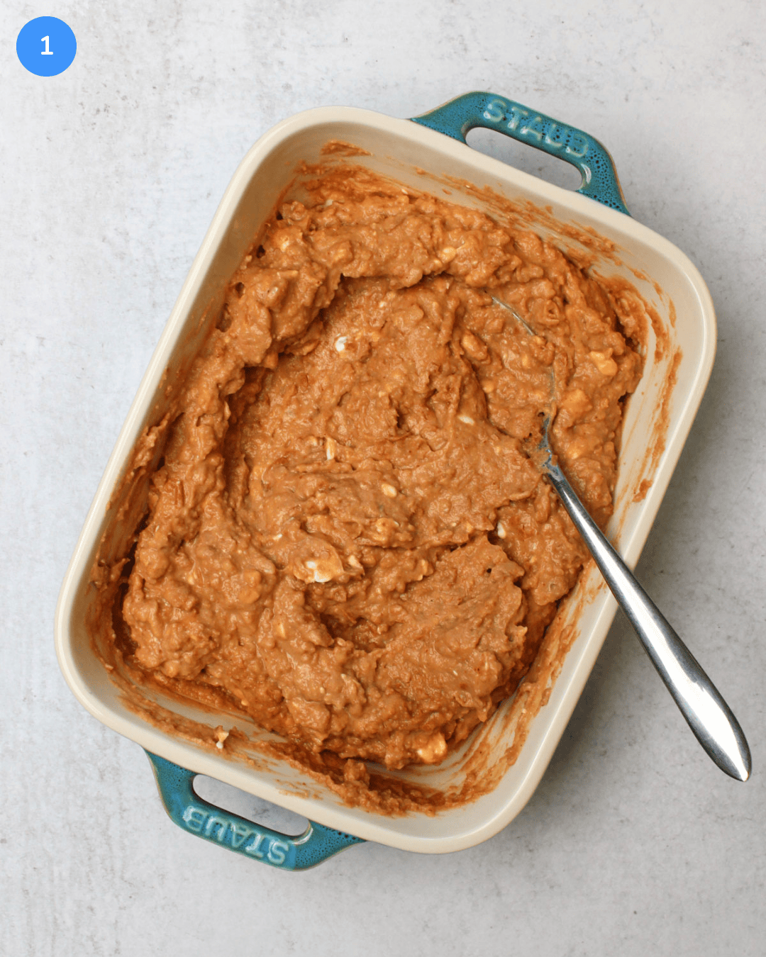 A small ceramic baking dish with a refried bean and cream cheese mixture in it.