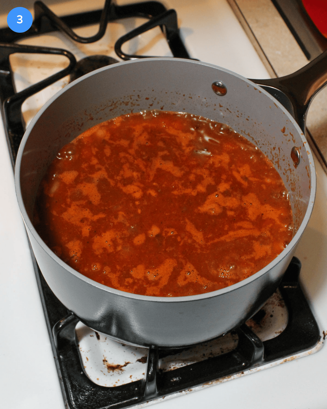 A ceramic saucepot with freshly made ranchero sauce simmering in it on the stove.