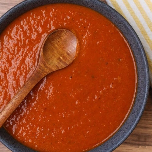A stoneware bowl filled with freshly cooked ranchero sauce and a wooden serving spoon.