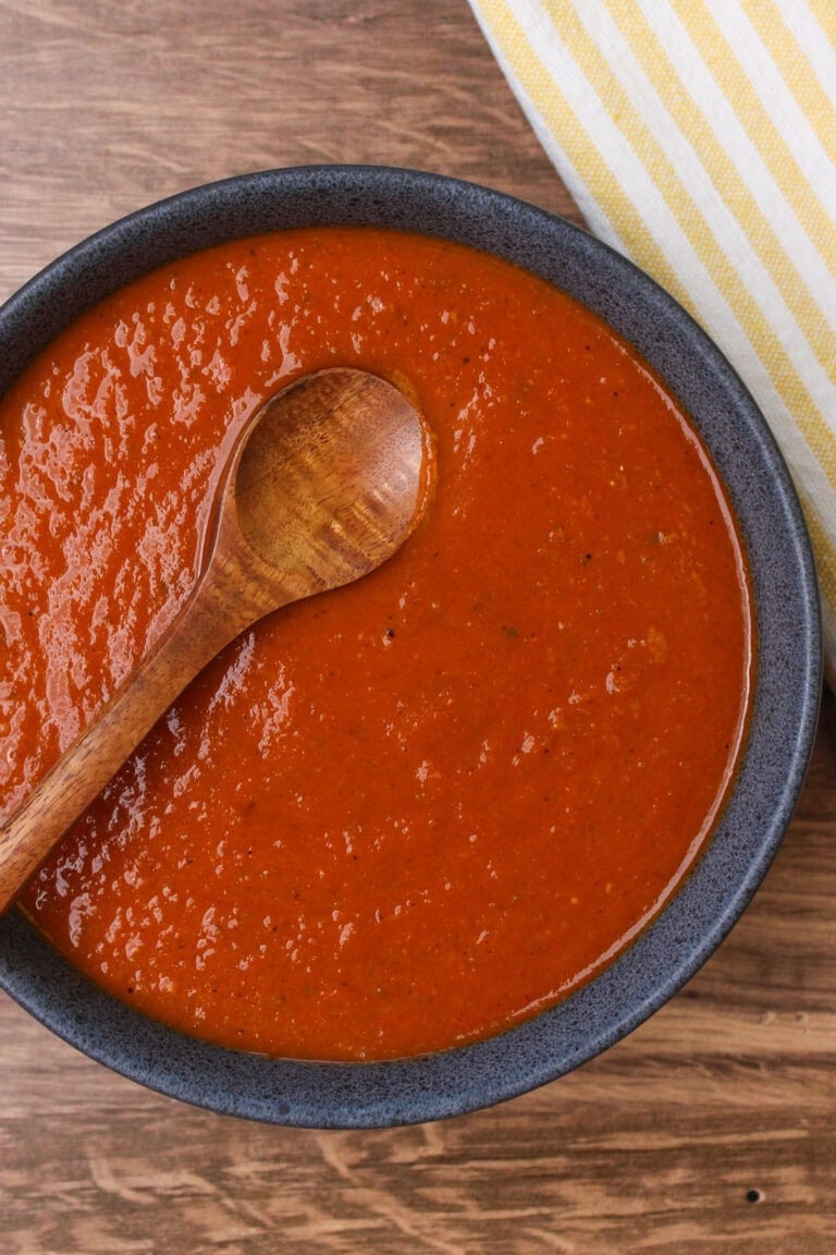 A stoneware bowl filled with freshly cooked ranchero sauce and a wooden serving spoon.