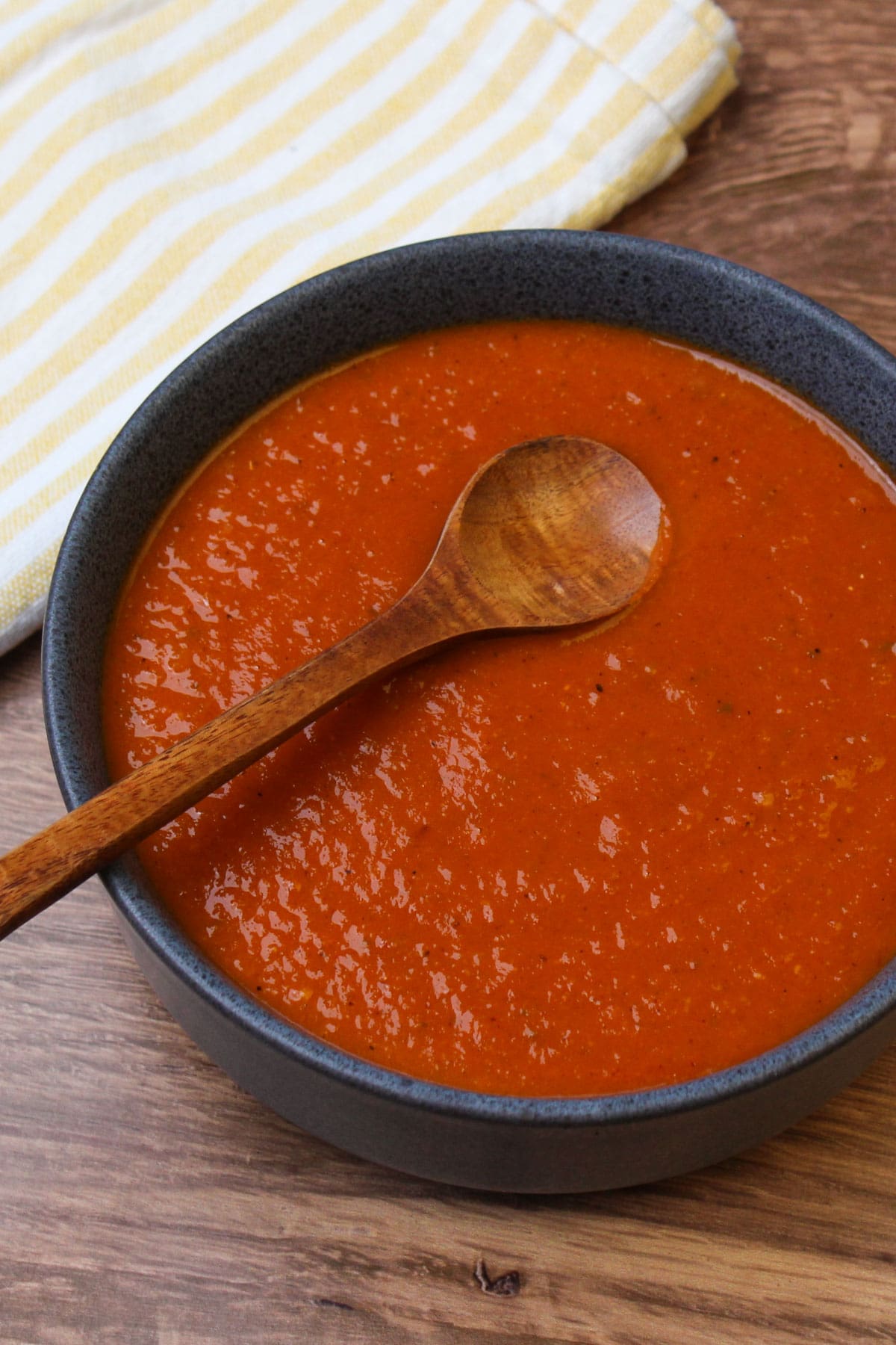 A blue stoneware bowl filled with a fresh batch of homemade ranchero sauce and a wooden serving spoon.